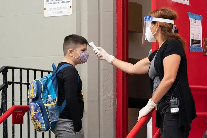 A young boy wearing a backpack and mask has his temperature taken before entering PS 179 elementary school in Kensington, Brooklyn.
